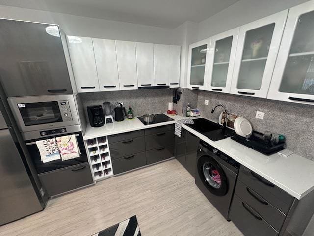 Современная кухня с серыми и белыми шкафами, техникой и стильной отделкой, располагающая к уютному приготовлению пищи.