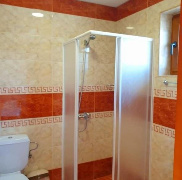 Современная ванная комната с душевой кабиной, унитазом и керамической плиткой в теплых оттенках красного и бежевого.