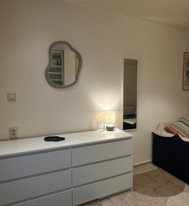 Современный интерьер студии с белым комодом, зеркалом и уютным текстилем на диване. Светлые тона и минимализм.