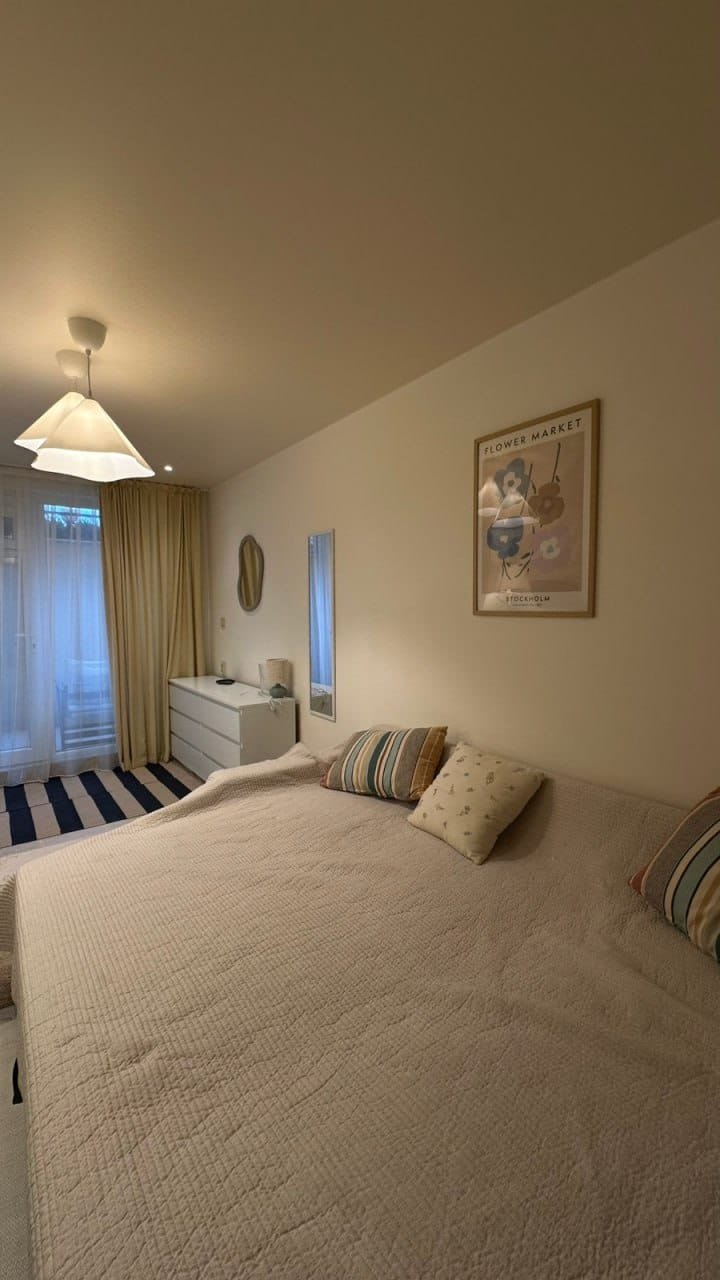 Современная студия с мягким угловым диваном, светлыми тонами, минималистичной мебелью и уюта создающим освещением.