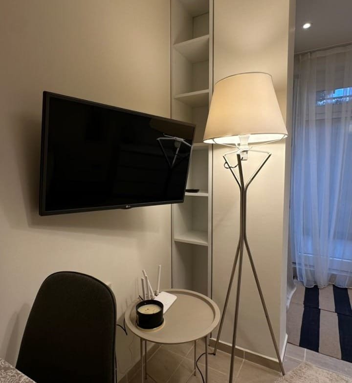 Современная студия с телевизором, напольной лампой и столиком, оформленная в нейтральных тонах и с уютным освещением.