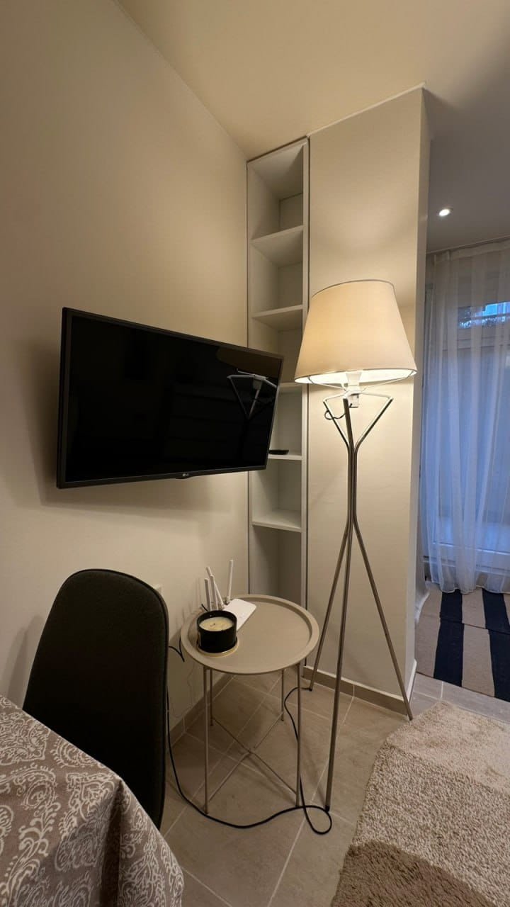 Современная студия с телевизором, напольной лампой и столиком, оформленная в нейтральных тонах и с уютным освещением.