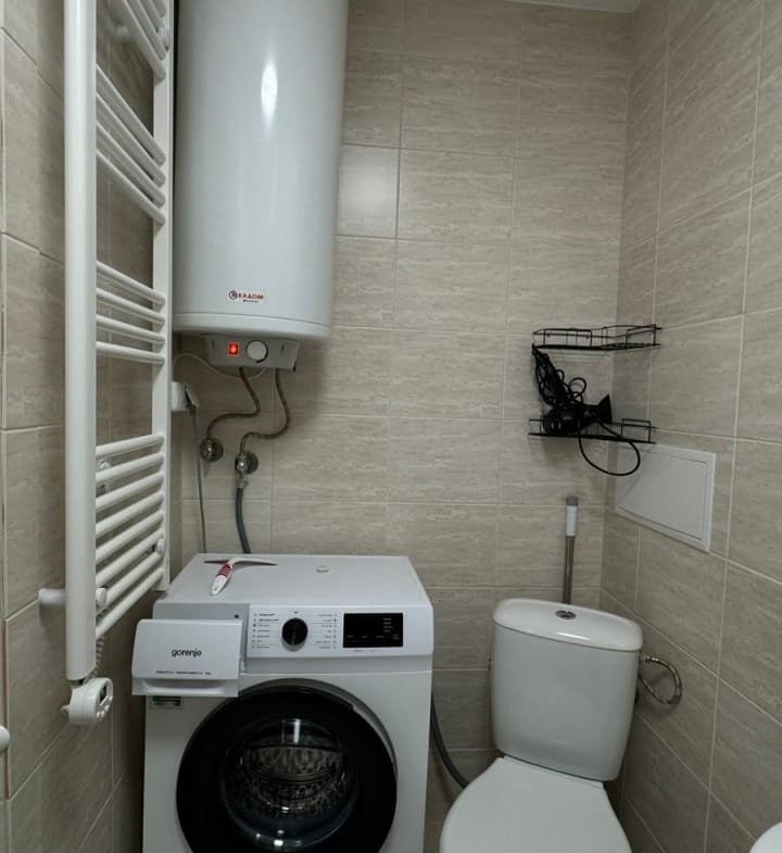 Современная ванная комната с унитазом, стиральной машиной и полотенцесушителем на светлом фоне.