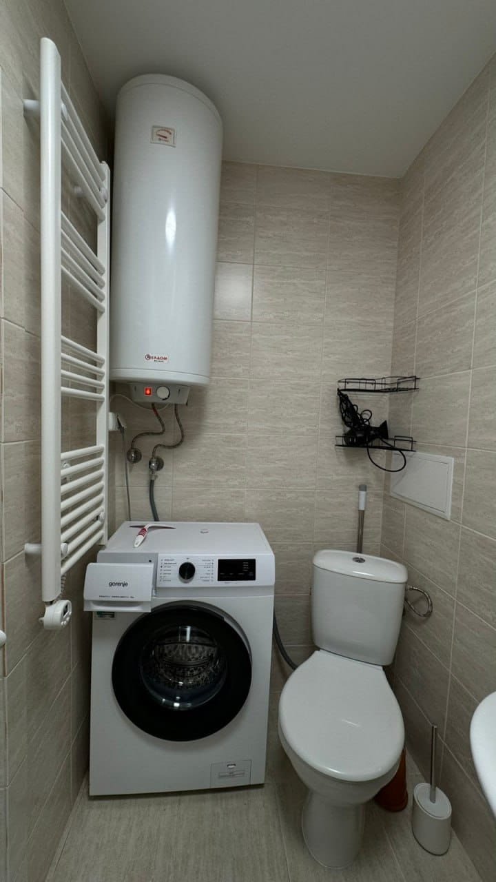 Современная ванная комната с унитазом, стиральной машиной и полотенцесушителем на светлом фоне.