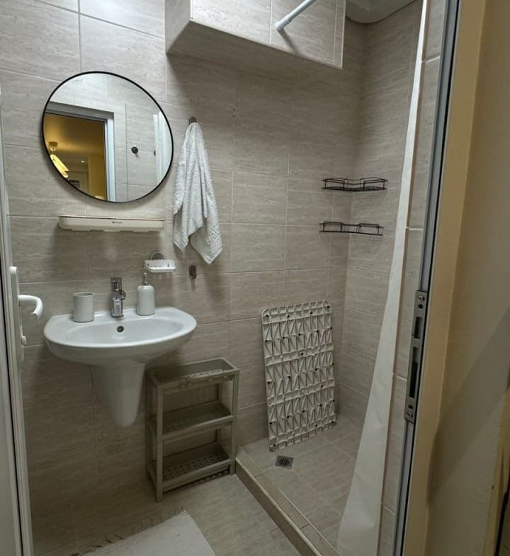 Современная ванная комната в студии, светлые стены, раковина, зеркало, душевая кабина и аккуратные полки.