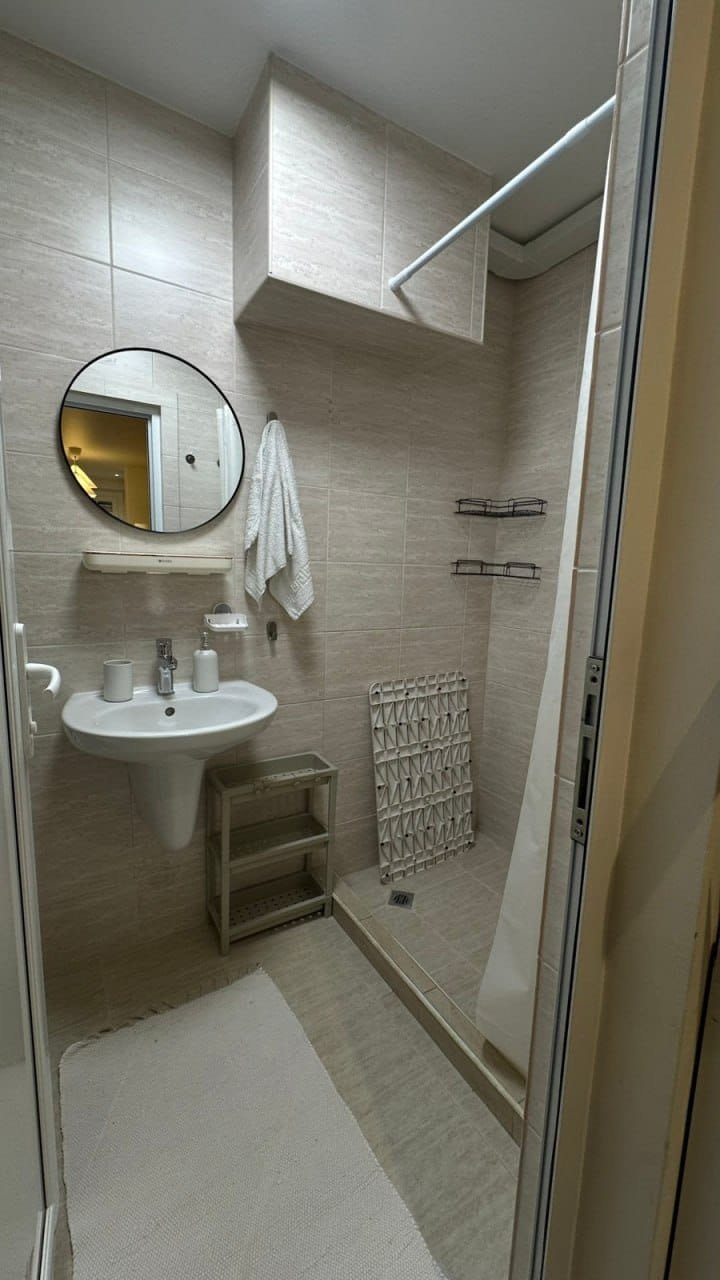 Современная ванная комната в студии, светлые стены, раковина, зеркало, душевая кабина и аккуратные полки.