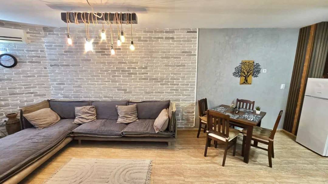 Современный интерьер двухкомнатного апартамента, светлая гостиная с диваном, обеденный стол и акцентная стена из кирпича.
