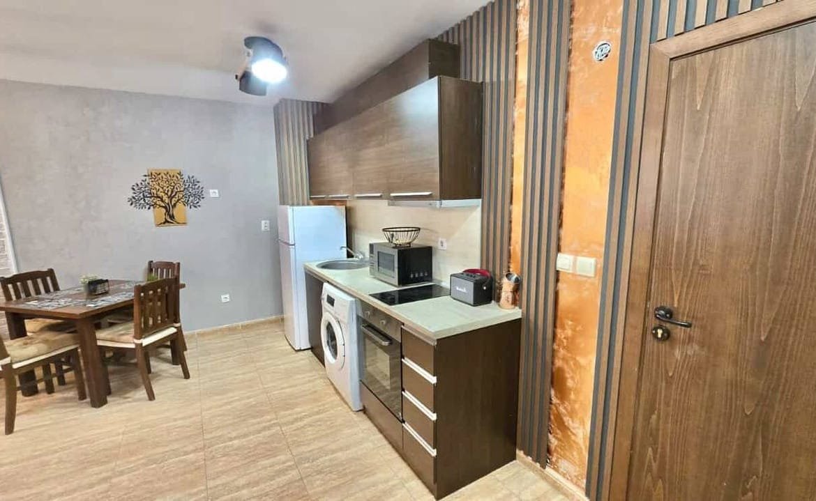 Современная кухня с деревянными фасадами, обеденный стол, стиральная машина и бытовая техника. Теплые тона и стильный декор.