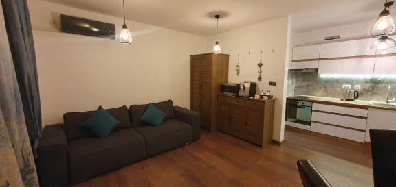 Современная студия с уютным диваном, кофейным столиком и кухней, оформленная в светлых тонах.