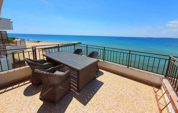 Терраса с плетеными креслами и столом, вид на море и пляж, ясное небо и солнечная погода.