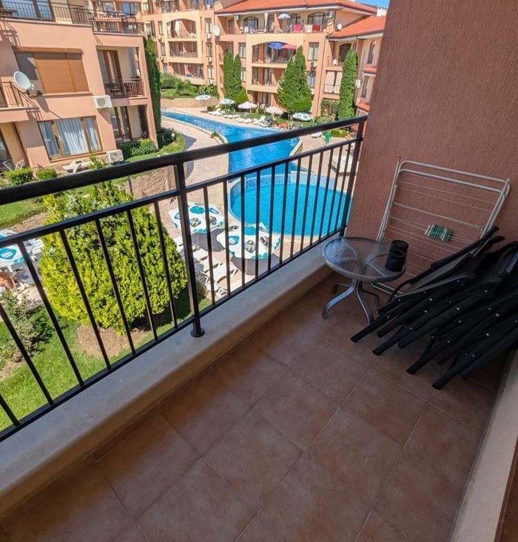 Балкон с видом на бассейн и зелёные насаждения комплекса Panorama Dreams, стулья и столик на плиточном покрытии.