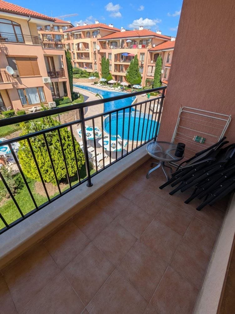 Балкон с видом на бассейн и зелёные насаждения комплекса Panorama Dreams, стулья и столик на плиточном покрытии.