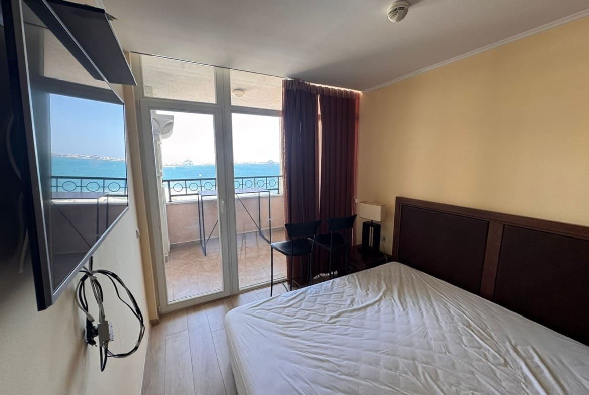 Современный интерьер трехкомнатного апартамента с балконом, видом на море и телевизором на стене.