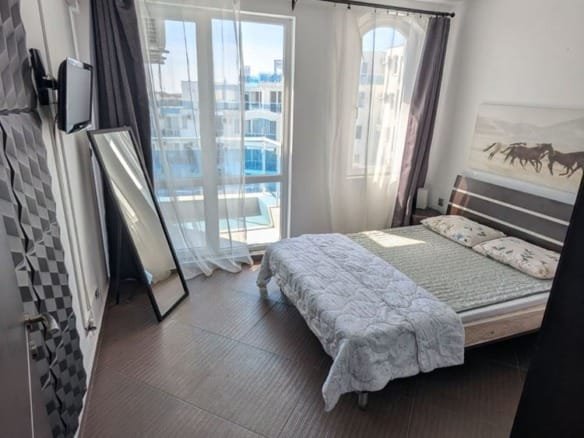 Современный двухкомнатный апартамент с крупными окнами, светлым интерьером и удобной спальней с кроватью и зеркалом.