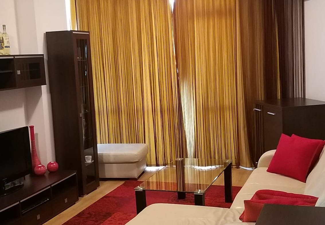 Современный интерьер двухкомнатного апартамента: светлая гостиная с диваном, столом, красными акцентами и большими окнами с занавесками.