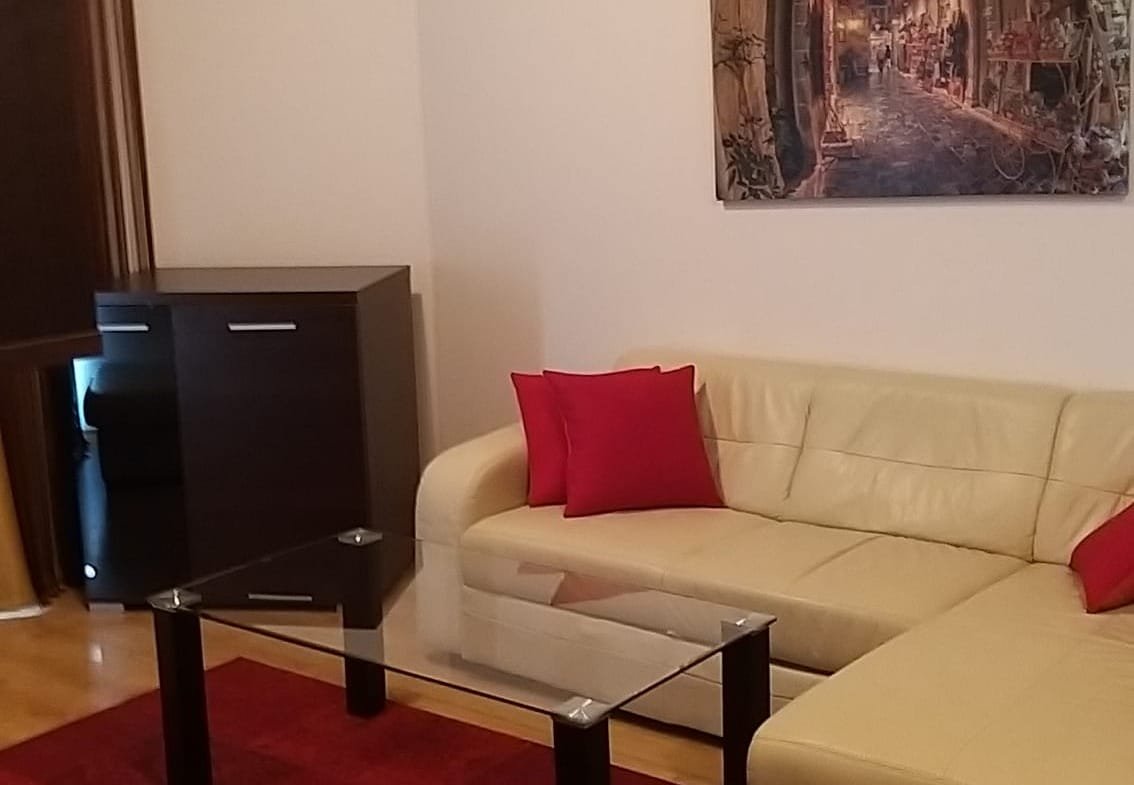 Современный интерьер двухкомнатного апартмента: светлый диван, красные подушки, оригинальная картина и стильный журнальный столик.