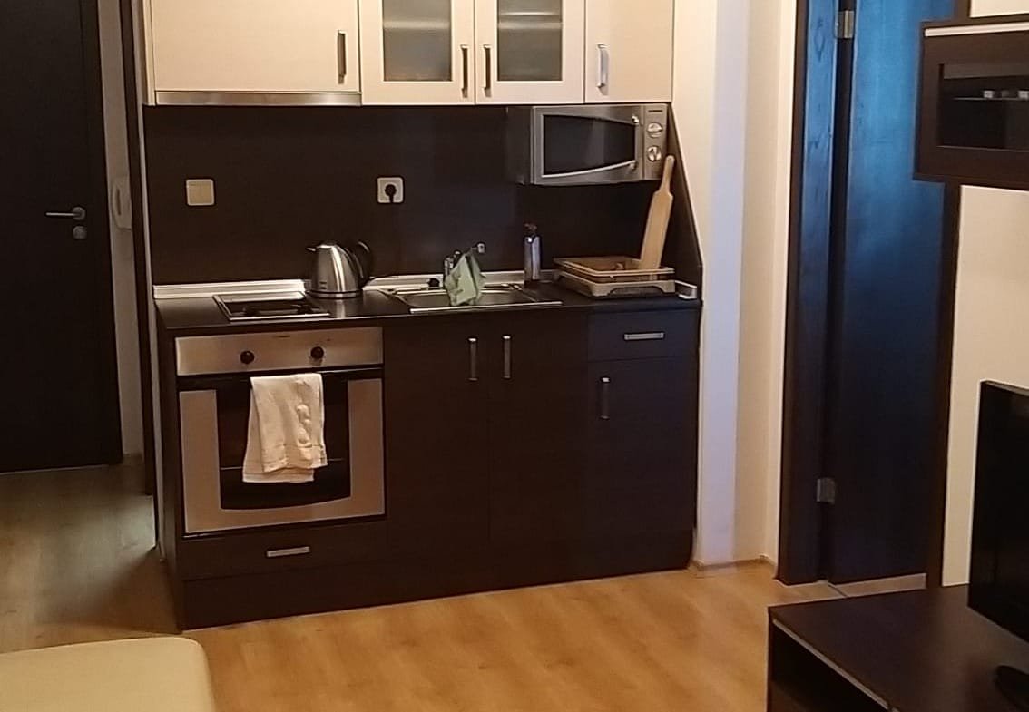 Современная кухня с плитой, микроволновкой и стильными шкафчиками, выполненная в светлых тонах с деревянным полом.