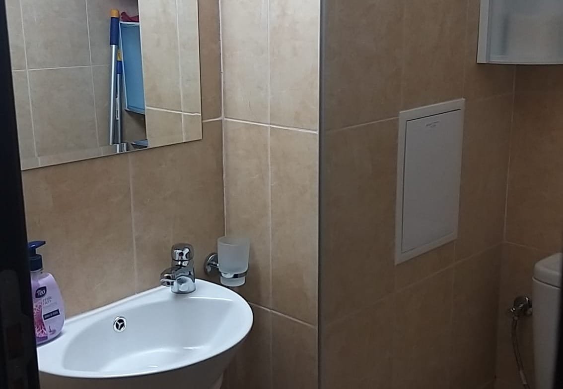 Современная ванная комната с унитазом, раковиной и зеркалом на стене, отделка из светлой плитки.