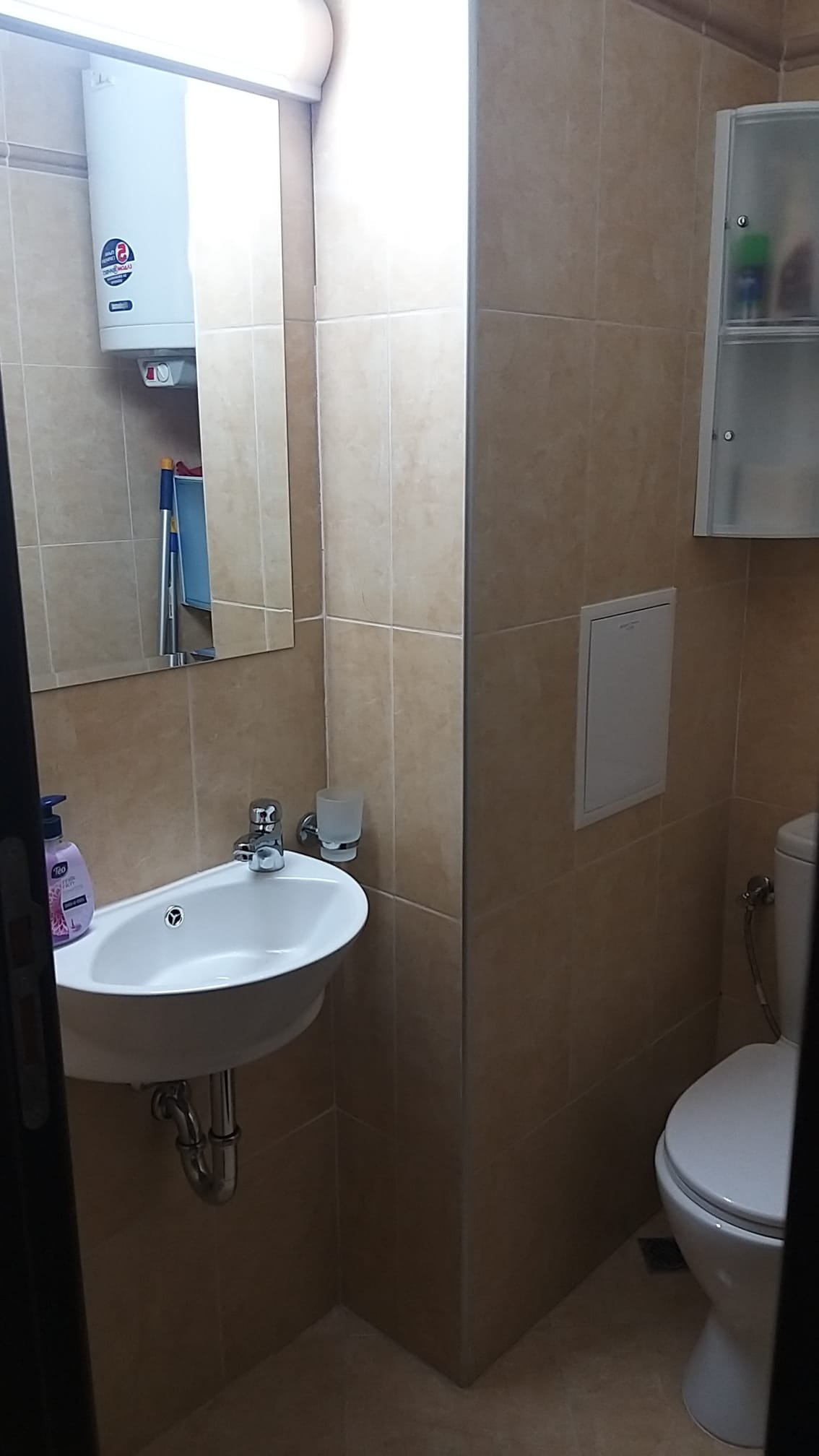 Современная ванная комната с унитазом, раковиной и зеркалом на стене, отделка из светлой плитки.