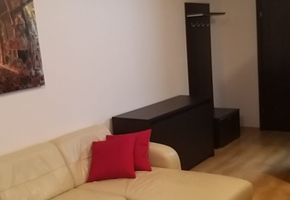 Уютная гостиная с кожаным диваном, красной подушкой и стеклянным столом, организованная для комфортного отдыха.