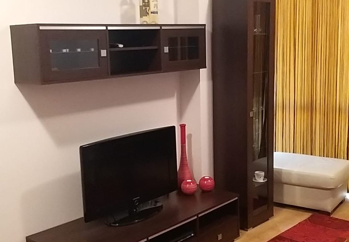 Современный интерьер двухкомнатного апартамента: телевизор, стенка из темного дерева, красные акценты и уютный диван.