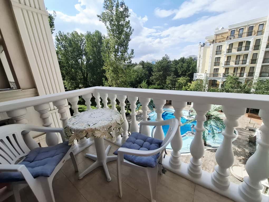 Балкон трехкомнатного апартамента с креслом и круглым столом, вид на зеленый двор и бассейн комплекса.