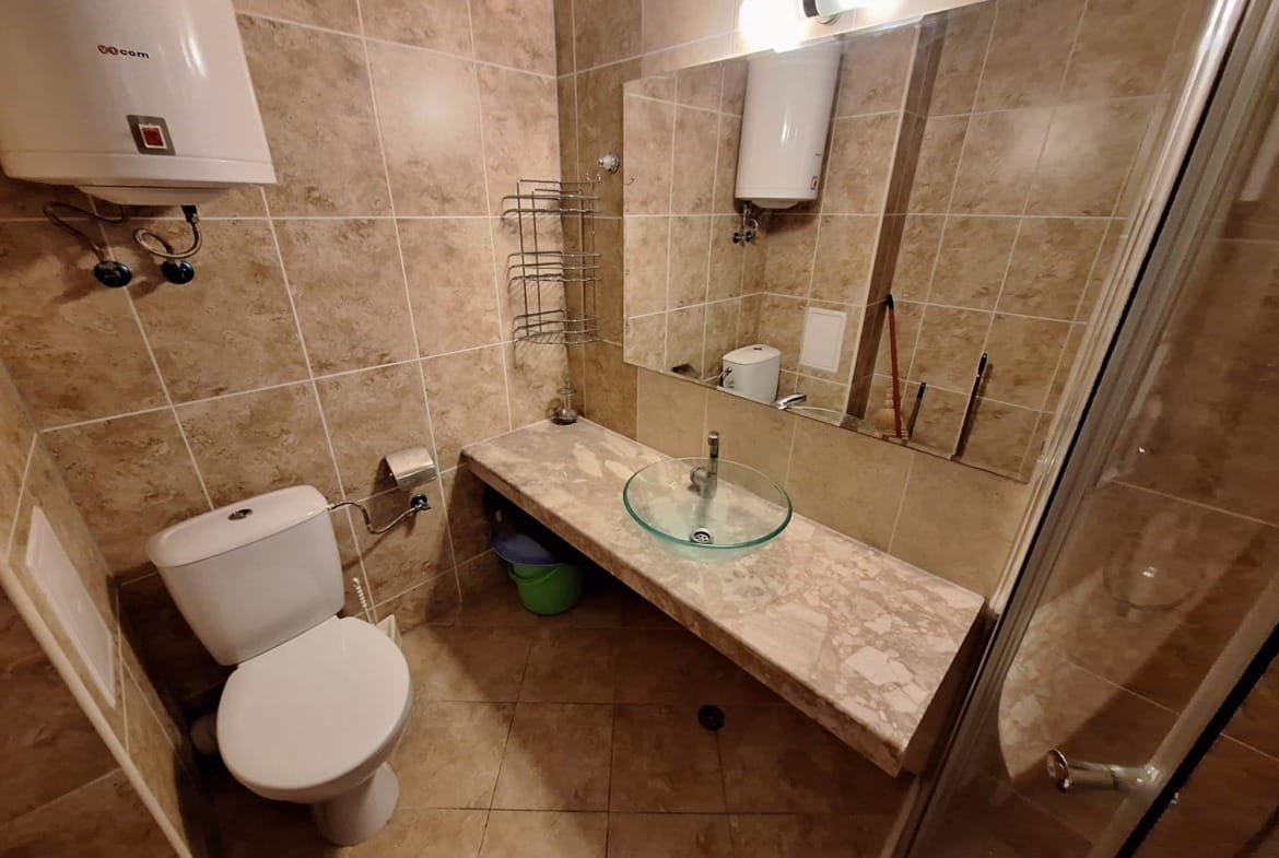 Современный санузел с плиткой в бежевых тонах, стеклянной раковиной и душевой кабинкой. Удобное оформление и чистота.