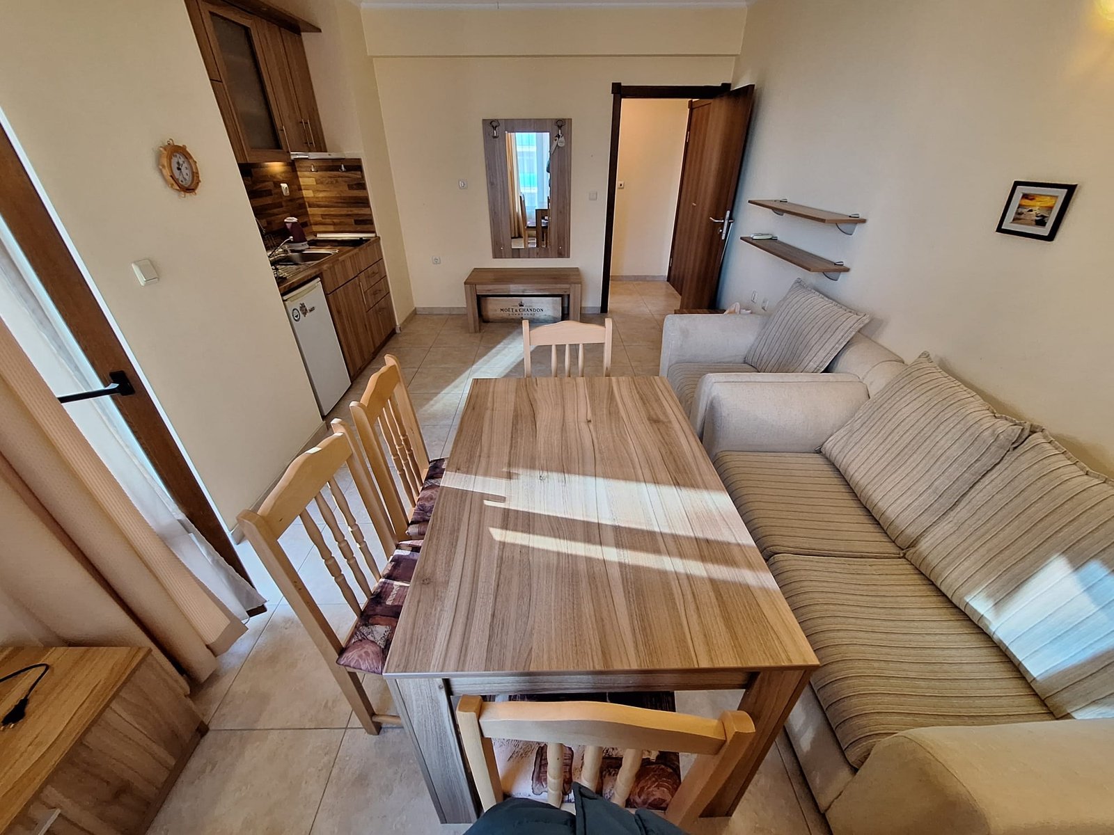 Уютный двухкомнатный апартамент с кухонной зоной, столом, диваном и зеркалом, оформленный в светлых тонах.