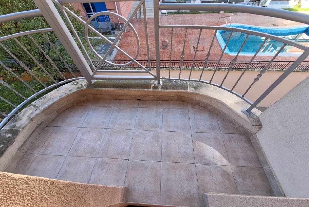 Балкон с плиточным покрытием и металлоконструкцией, выходящий на бассейн и зелёные насаждения.