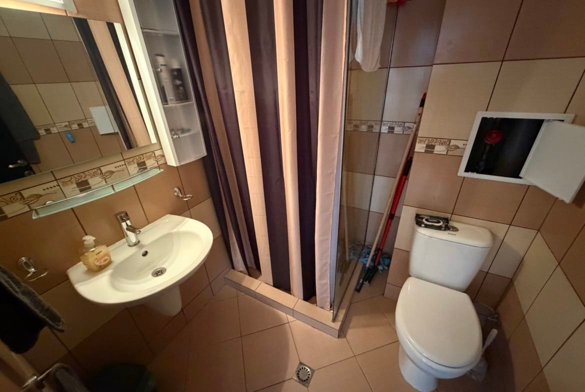 Санузел с душевой занавеской, умывальником и унитазом, отделка плиткой, простое освещение и минималистичный дизайн.