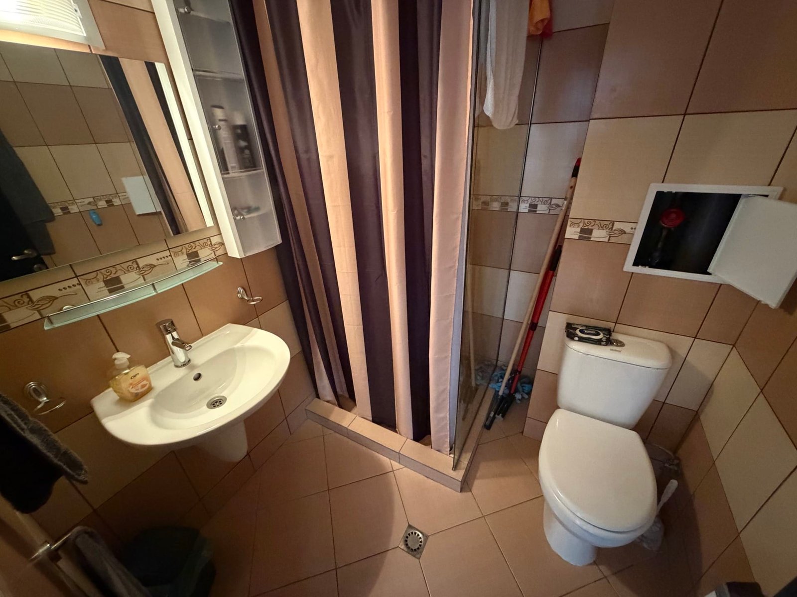 Санузел с душевой занавеской, умывальником и унитазом, отделка плиткой, простое освещение и минималистичный дизайн.