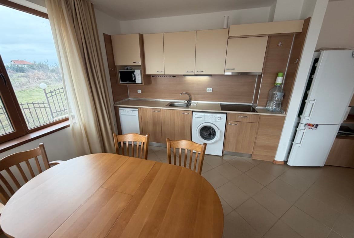 Современная кухня с деревянным столом и стульями, с техникой, включая стиральную машину и посудомойку.