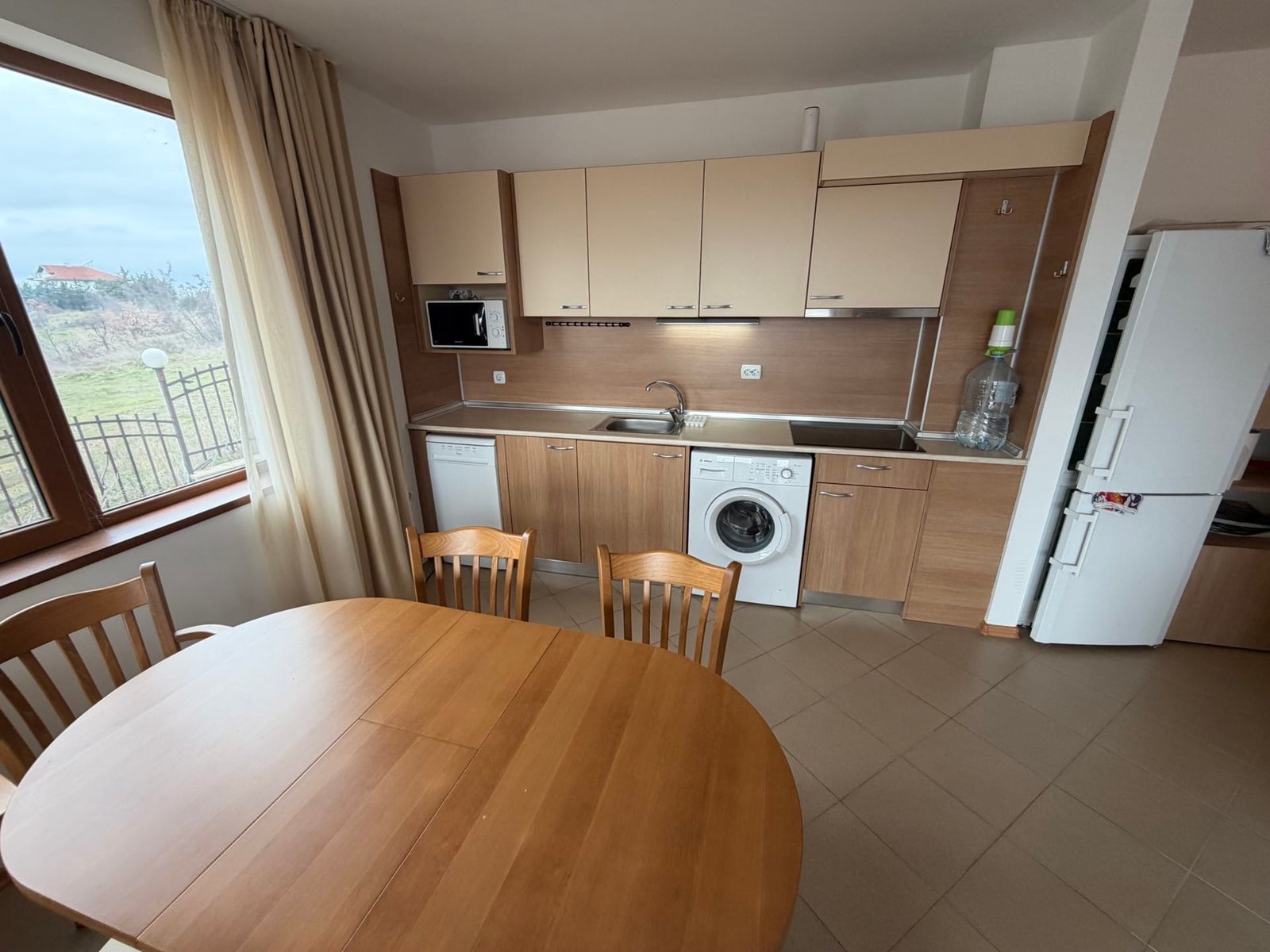 Современная кухня с деревянным столом и стульями, с техникой, включая стиральную машину и посудомойку.