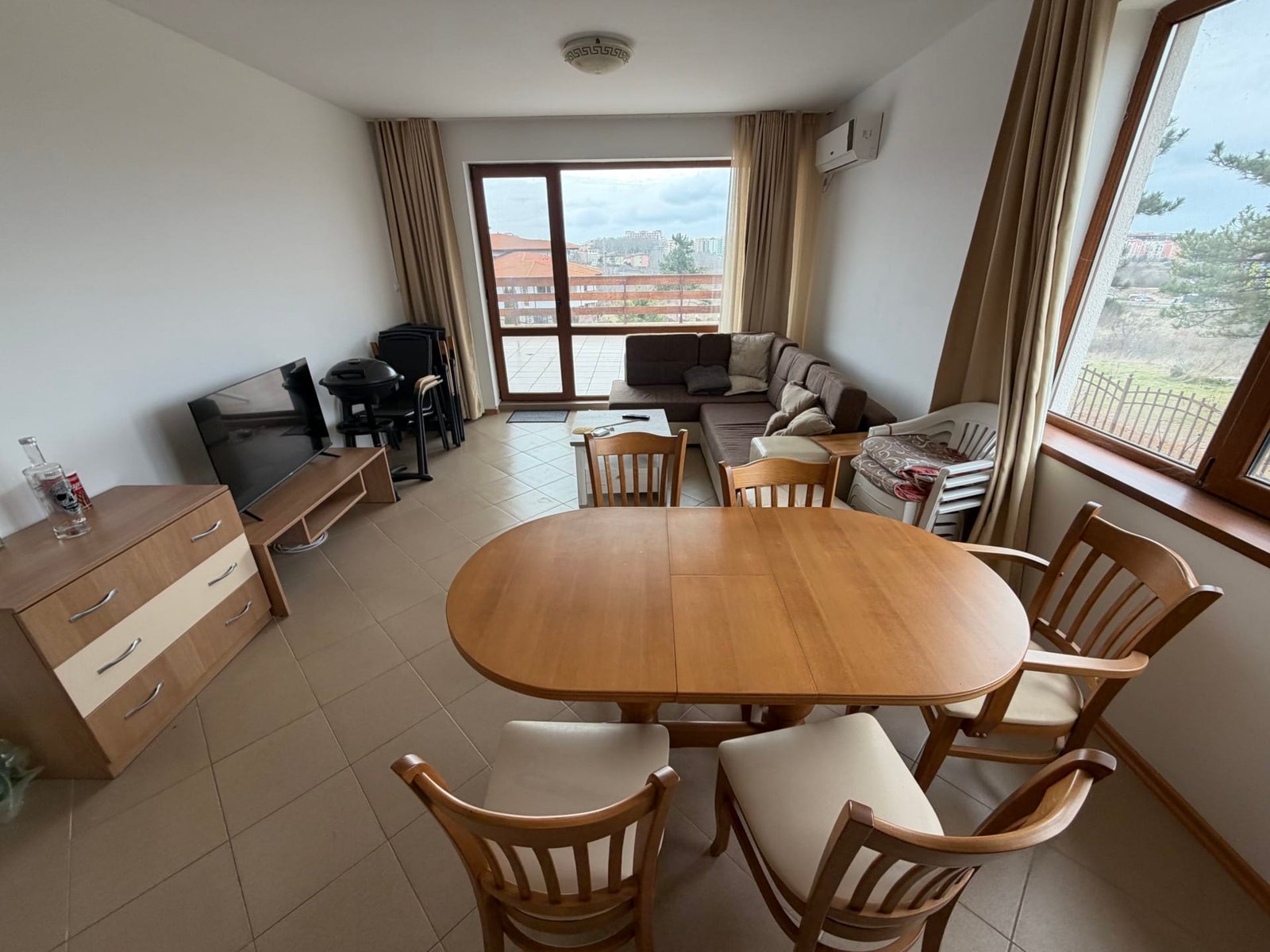 Современный интерьер трехкомнатной квартиры с обеденной зоной, угловым диваном, телевизором и большим окном.