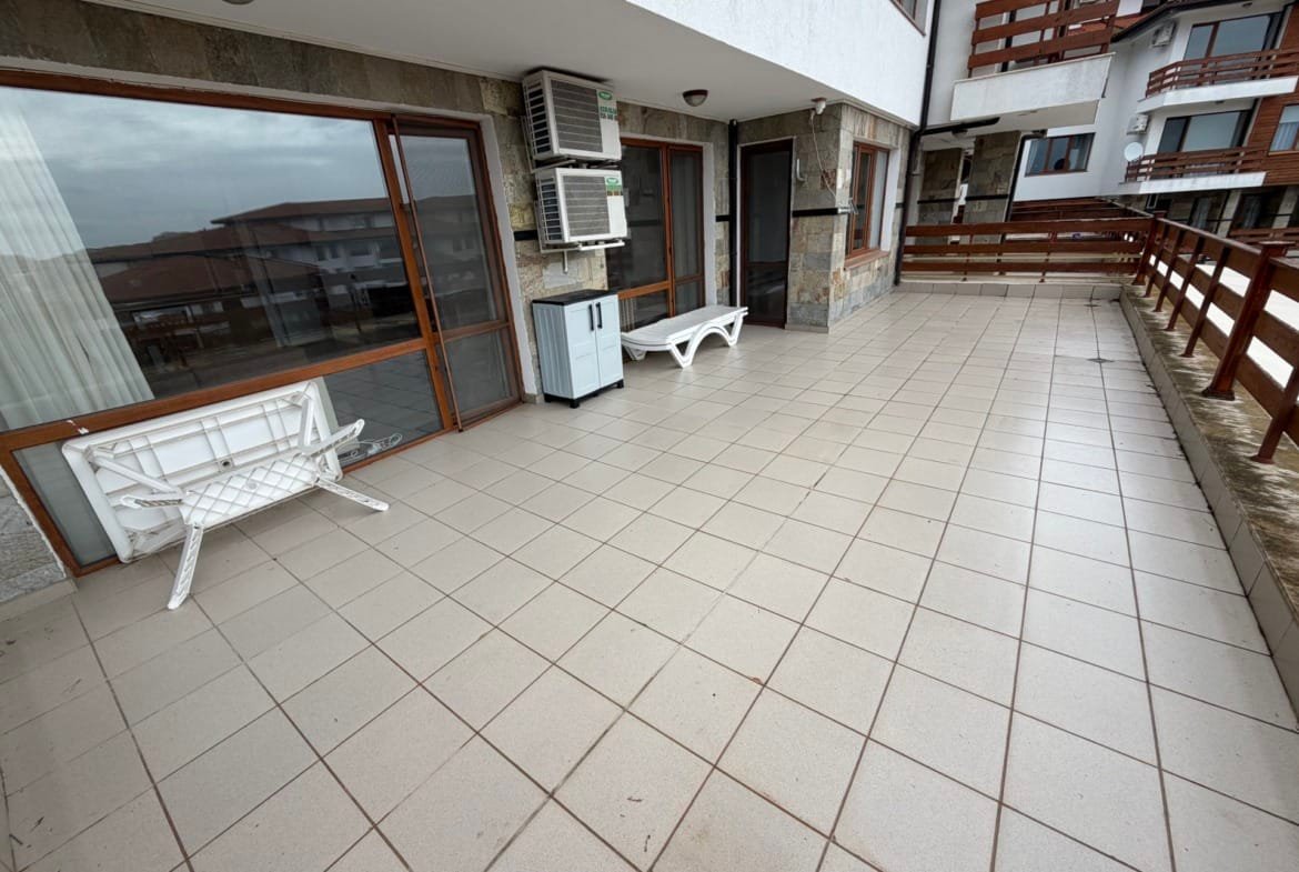 Просторная терраса с плиткой, белыми стульями и деревянным ограждением в комплексе Gardenia Hills.