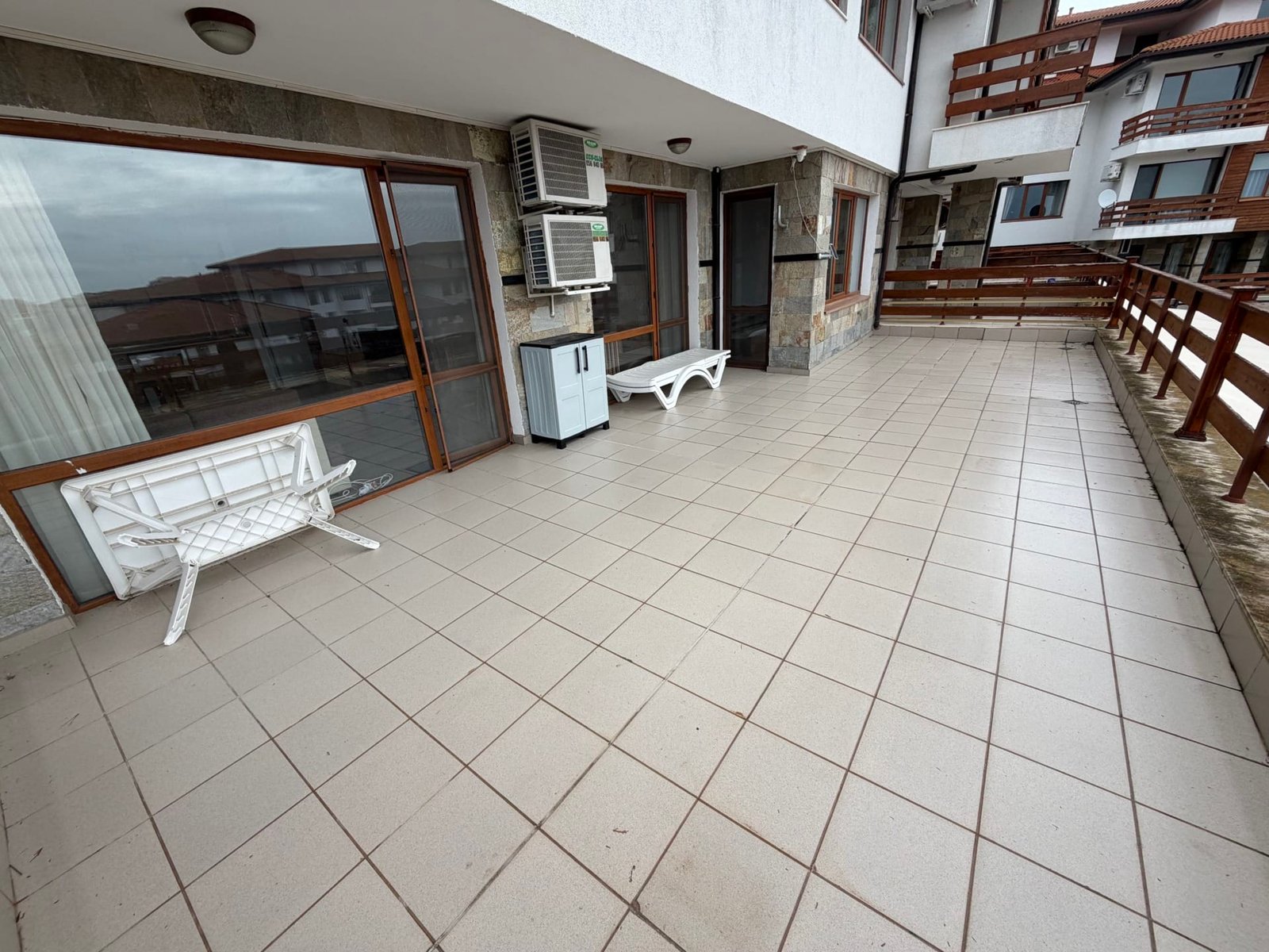 Просторная терраса с плиткой, белыми стульями и деревянным ограждением в комплексе Gardenia Hills.