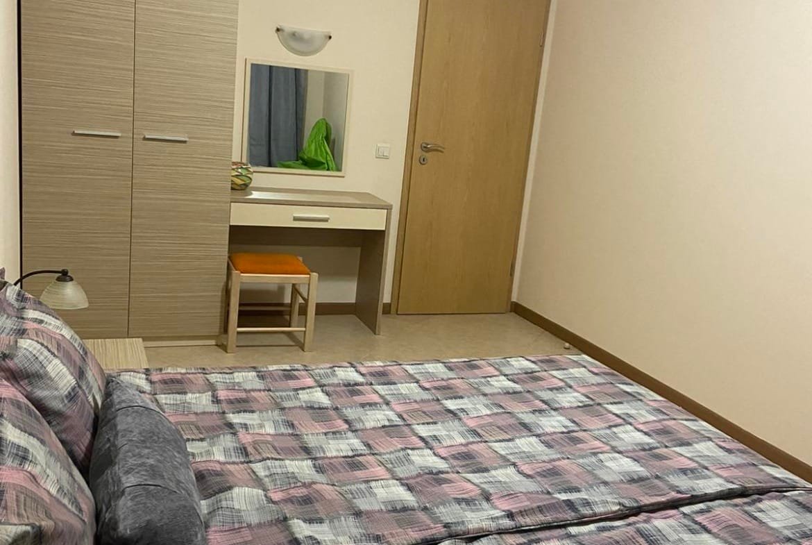 Современная двухкомнатная квартира с двуспальной кроватью, комодом и зеркалом в светлых тонах.