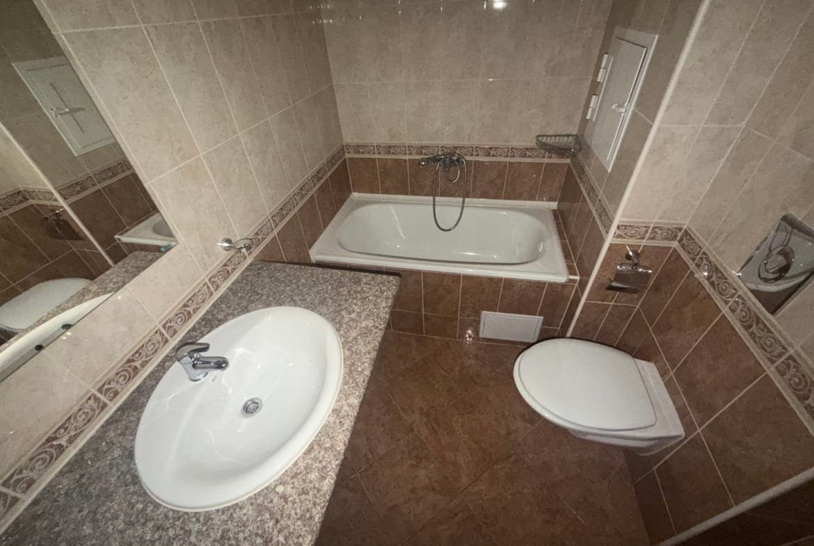 Современная ванная комната с ванной, раковиной и унитазом, отделанная плиткой светлых тонов и коричневыми акцентами.