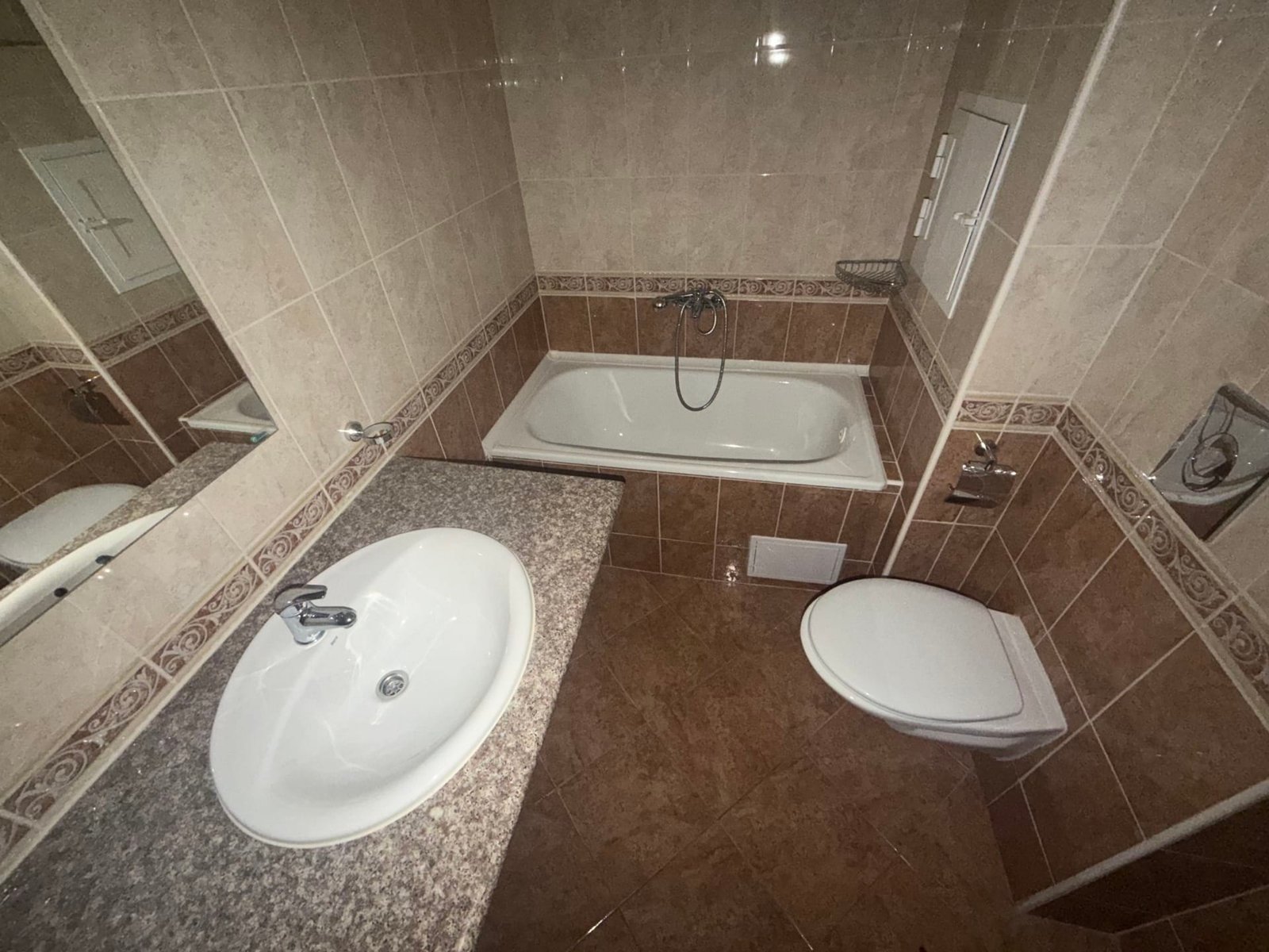 Современная ванная комната с ванной, раковиной и унитазом, отделанная плиткой светлых тонов и коричневыми акцентами.