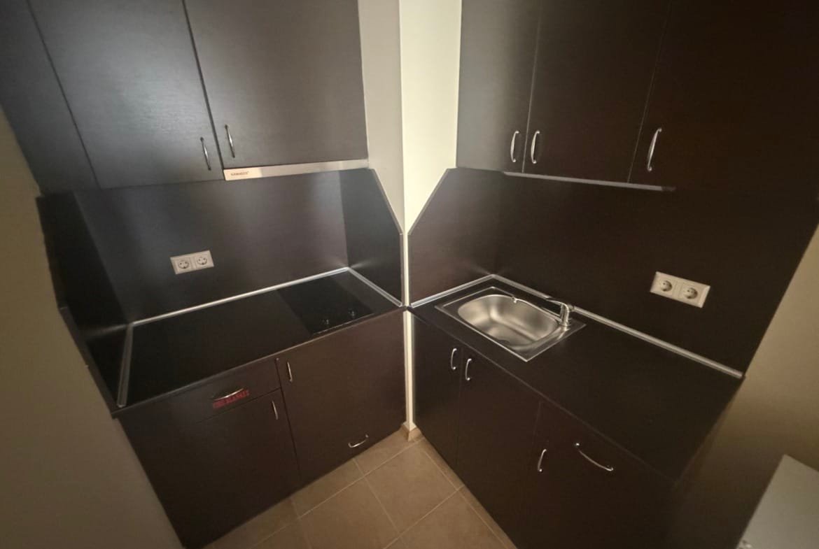 Современная кухня в апартаменте: темные древесные фасады, встроенная плита и мойка, минималистичный дизайн.