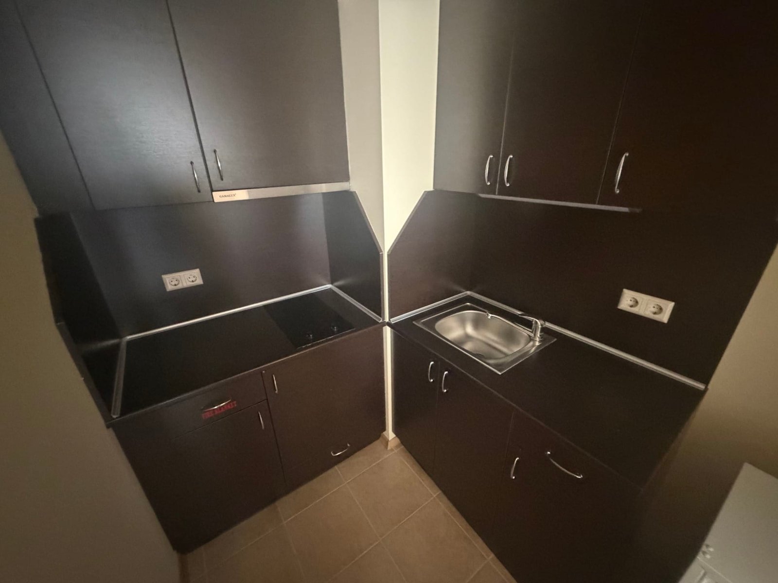 Современная кухня в апартаменте: темные древесные фасады, встроенная плита и мойка, минималистичный дизайн.