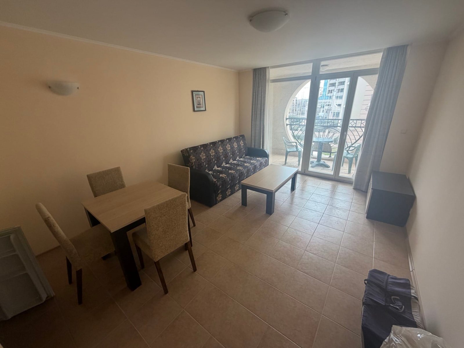 Двухкомнатный апартамент с диваном, столом и стульями, светлые стены и большие окна с видом на балкон.