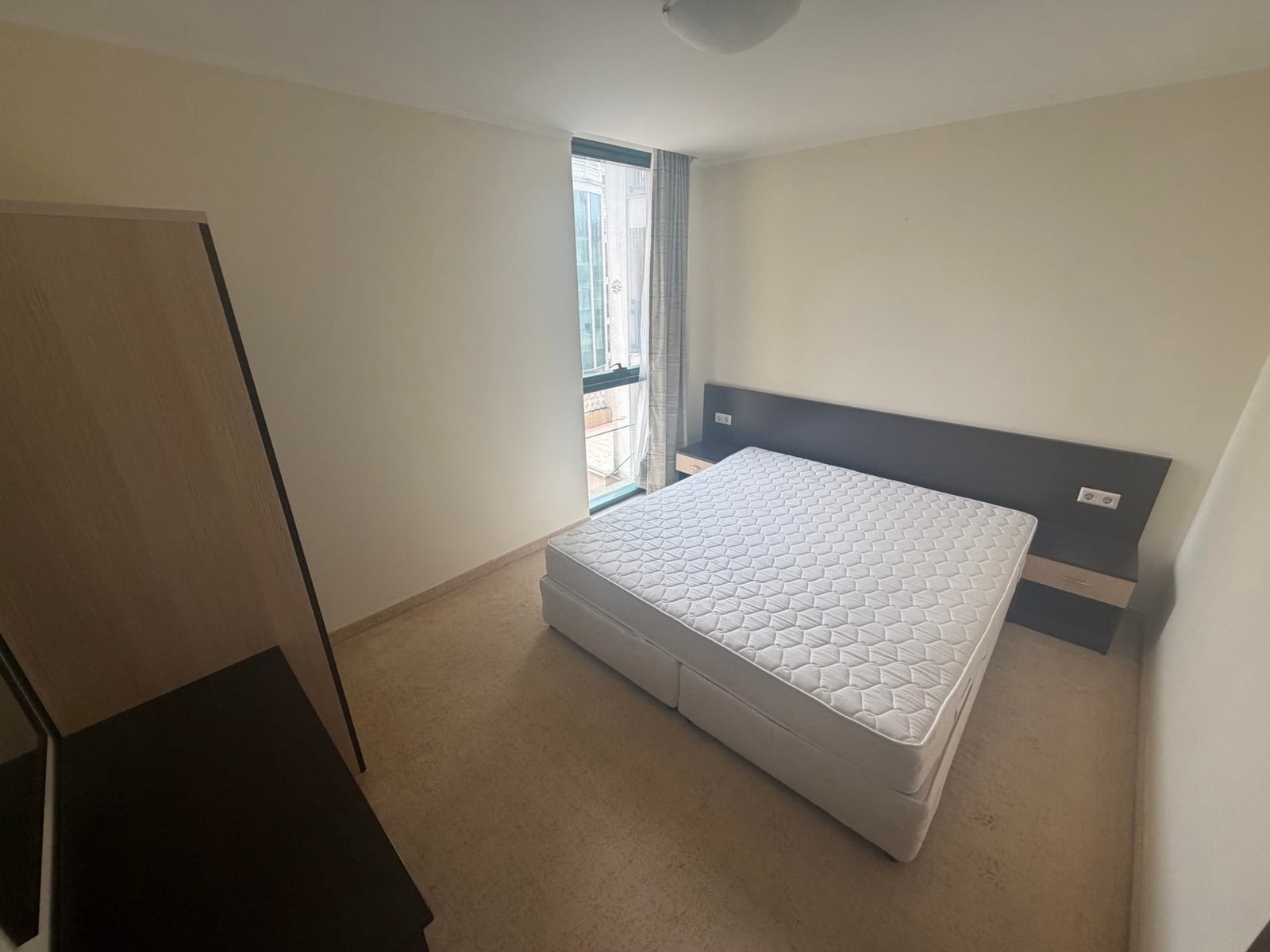 Современная спальня с двуспальной кроватью и окнами, обеспечивающими естественное освещение, в апартаменте у моря.