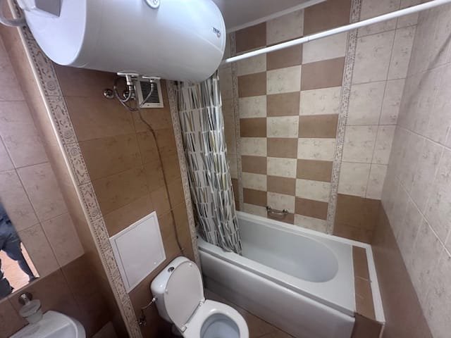 Современная ванная комната с ванной, унитазом и душевой занавеской, оформленная в светлых и коричневых тонах.