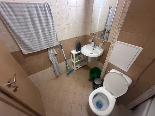 Современный санузел с унитазом, раковиной и хранилищем, оформленный в светлых тонах и плитке.