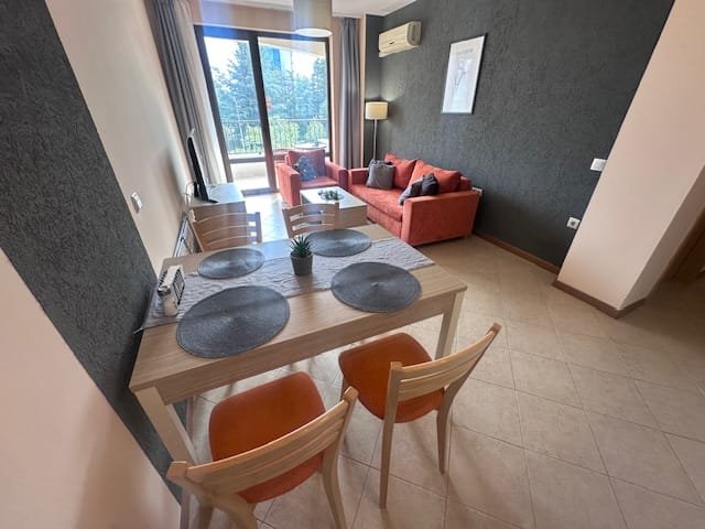 Современный двухкомнатный апартамент с уютной гостиной, столом для обеда и балконом, оформленный в светлых тонах.