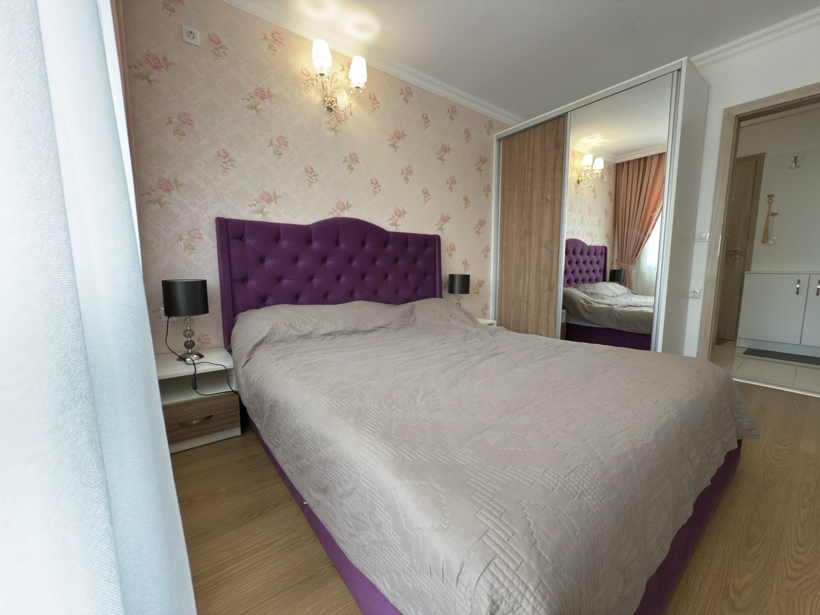 Современная спальня с коричневым наполовину прикрытым постельным бельём и фиолетовым изголовьем, отражающимся в зеркале.