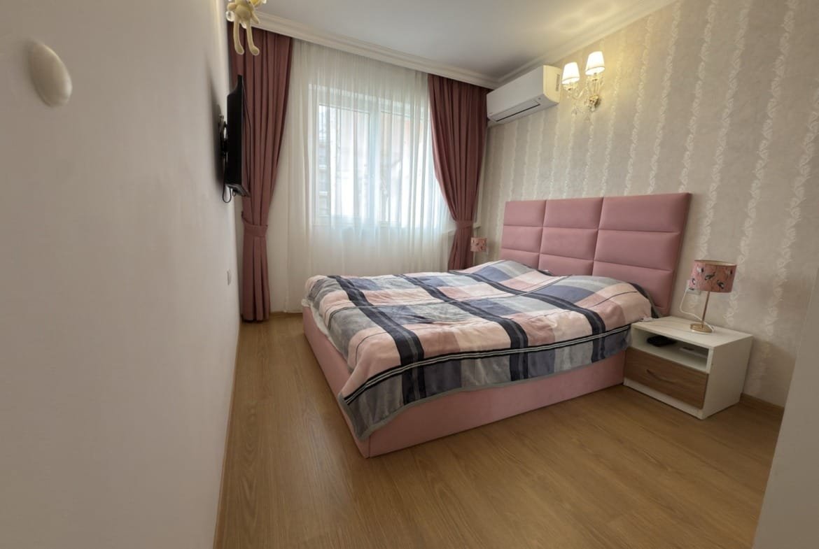 Современная спальня с розовой кроватью, стильным освещением и мягкими шторами, создающая уютную атмосферу.