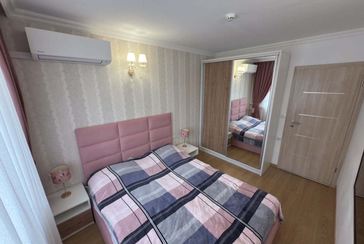 Современная спальня с двуспальной кроватью, мягкими тонами, зеркальным шкафом и светлыми шторами. Комфортное оформление.