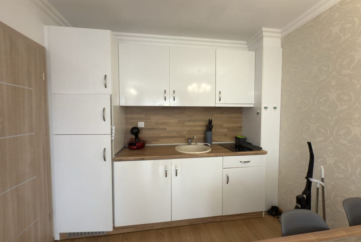 Современная кухня с белыми шкафчиками, деревянной столешницей, раковиной и кухонной техникой в апартаменте.